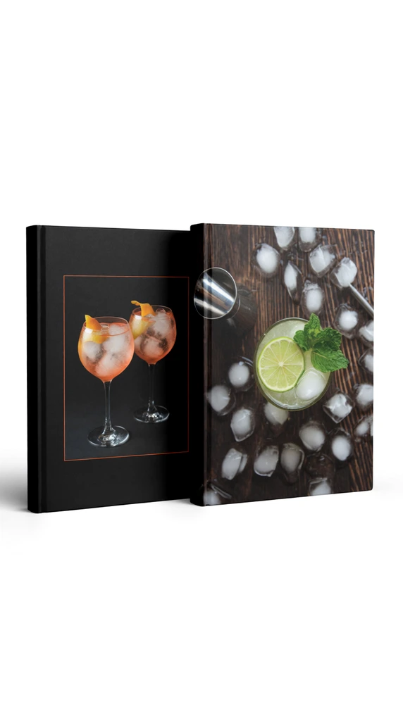 Two hardcover books stand upright on a seamless white studio surface. The left volume's black cover features a photograph of two ice-filled cocktails in balloon glasses garnished with citrus peels, framed by a thin orange line. The right volume displays a dark wood-grain cover showing a top-down view of a lime and mint cocktail surrounded by scattered ice cubes and silver bar tools. Soft lighting creates gentle shadows.