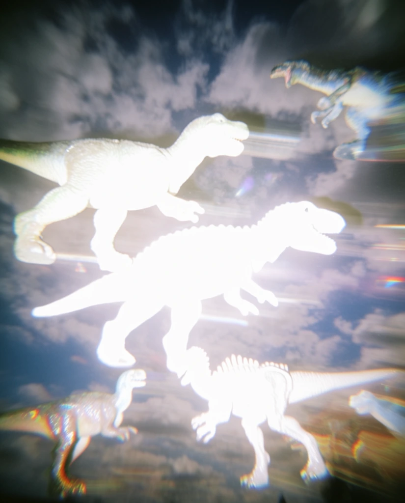Multiple toy dinosaurs float against a cloudy sky, captured with harsh direct flash photography and extreme overexposure. The primary dinosaurs appear as blown-out, glowing pure white silhouettes with intense light bloom and horizontal lens flares. Surrounding elements and clouds exhibit heavy directional motion blur, ghosting artifacts, and severe chromatic aberration along high-contrast edges. The overall aesthetic is chaotic and ethereal, characterized by low-resolution digital noise, camera shake, and an amateur Y2K digital camera visual quality.
