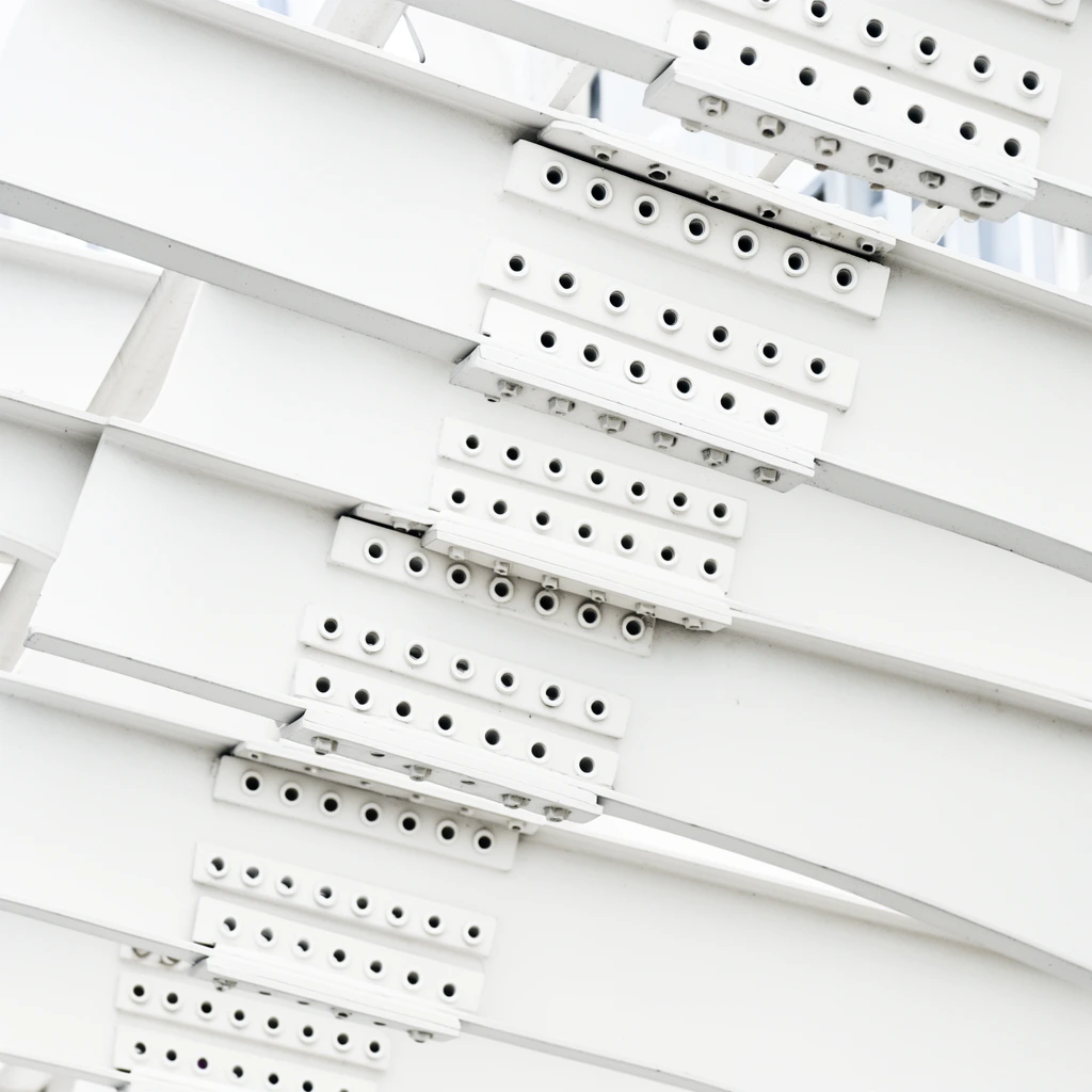 A stark close-up architectural study of layered white metal beams bolted together in an ascending pattern. Heavy, smooth rectangular plates overlap diagonally, each reinforced by raised strips containing precise rows of recessed circular bolt holes. Diffuse high-key lighting casts subtle shadows along the overlapping edges, emphasizing the minimalist monochromatic palette and rhythmic geometric repetition of the industrial hardware against a softly out-of-focus bright background.