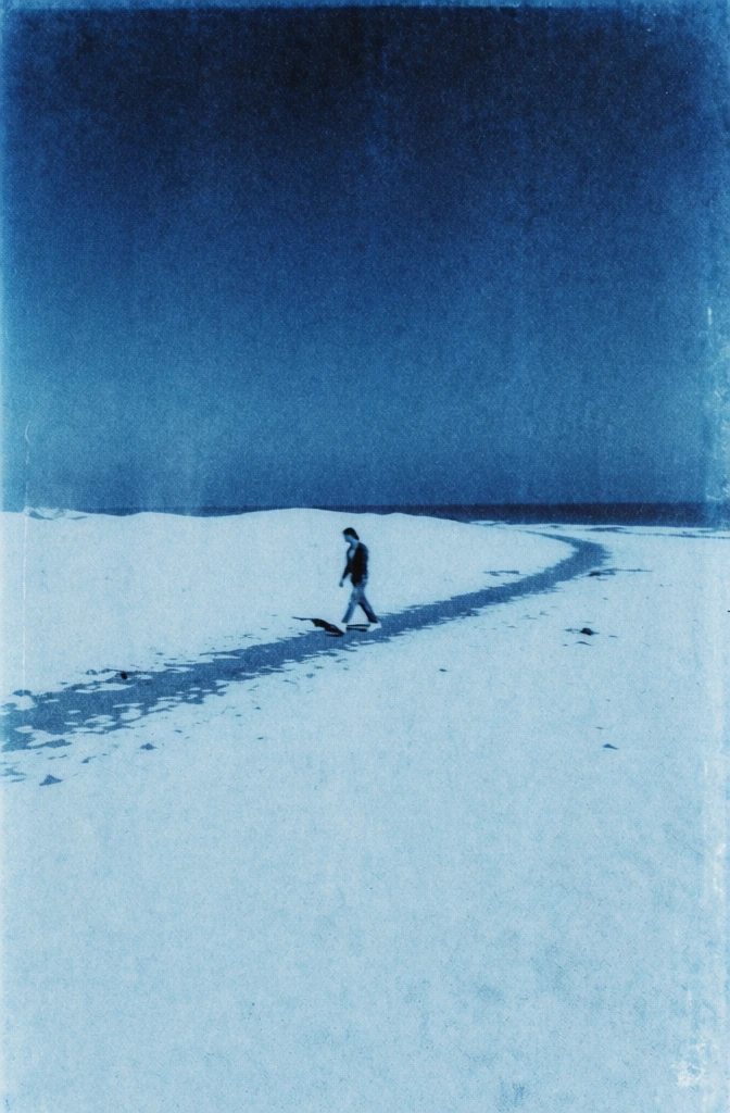 low-fidelity vintage analog film aesthetic, heavy photographic grain and gritty texture, monochromatic cyan and cerulean blue color palette with high contrast whites, a lone solitary figure walking along a narrow path covered in deep snow, minimalist vertical composition, grainy risograph print quality, cold and nostalgic atmosphere, soft diffused lighting, fine grit and noise throughout, desaturated highlights, cinematic atmospheric perspective, dreamy lo-fi aesthetic.