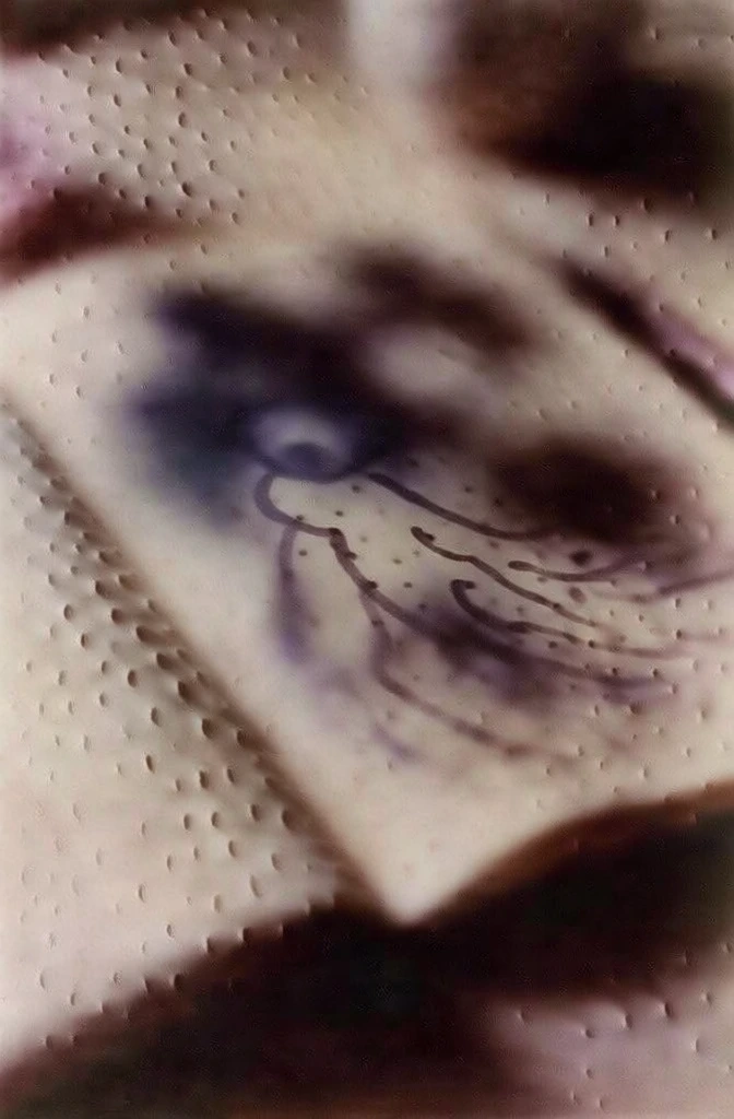 top-down view of an open notebook on a weathered dark wood desk, ethereal soft-focus hazy atmosphere, muted cream and deep violet tones, tactile dimpled texture with small indentations across the entire frame, loose marker drawings of a cosmic space figure with fluid organic lines, cinematic bokeh, shallow depth of field, moody low lighting, vintage film grain, mysterious and atmospheric composition, grainy tactile surface, soft gradients of plum and beige, abstract shadows.