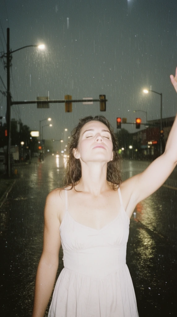 A woman stands in the center foreground, her eyes closed, head tilted back, and one arm raised, wearing a dress. Behind her stretches a wet street dotted with streetlights and traffic lights, with continuous rain falling throughout the scene. The composition is rendered in the style of raw, on-camera flash photography, characterized by harsh, direct, and flat frontal lighting that intensely illuminates the woman and freezes the falling raindrops as stark white highlights. The flash creates a high-contrast separation, causing the background street environment to recede into deeper shadows due to rapid light falloff, punctuated by the glowing ambient lights of the street fixtures reflecting on the wet pavement. The overall visual aesthetic mimics a 35mm film snapshot, featuring a muted, slightly desaturated color palette, visible film grain, and an unpolished, starkly lit editorial quality.