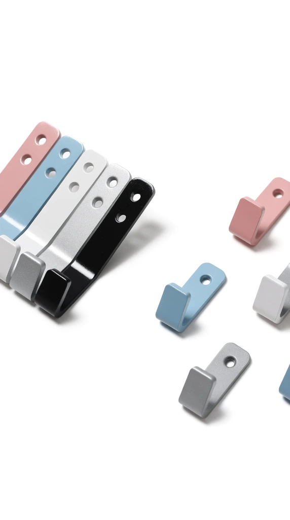 minimalist angled metal wall hooks on a stark white background, tight overlapping diagonal row of pink, light blue, white, textured silver, and glossy black hooks on the left, scattered matching hooks on the right, powder-coated finishes, dual mounting holes, soft directional studio lighting, subtle drop shadows, crisp contemporary product photography, high-angle perspective