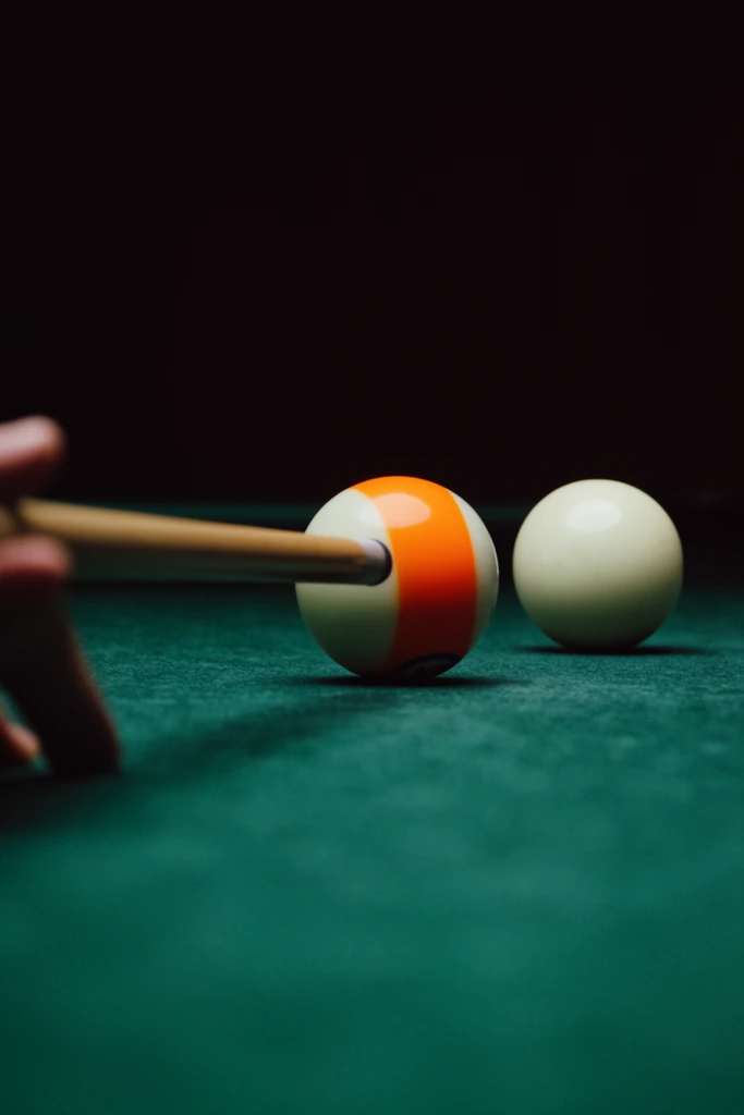 A low-angle, cinematic close-up of a billiard game set against a pitch-black background. A smooth wooden cue stick, guided by a partially obscured hand on the far left edge, is aimed squarely at an orange and white striped billiard ball. A solid white cue ball rests just to the right on a textured green felt surface. The composition features a striking shallow depth of field, blurring the foreground cue stick while keeping the brightly lit balls in focus. Moody, dramatic lighting casts soft curved highlights on the smooth spherical surfaces, emphasizing the rich contrast between the vibrant green table, the vivid orange stripes, and the deep dark expanse behind them.