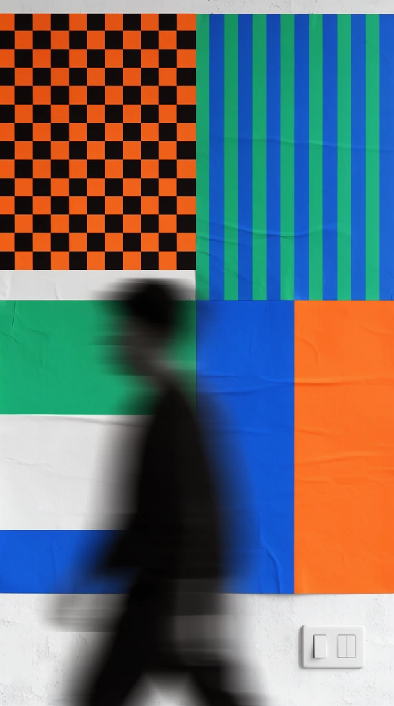 A heavily motion-blurred silhouette walks past a wall plastered with bold geometric posters. The flat, modernist graphic designs feature a high-contrast orange and black checkerboard, vibrant green and blue vertical stripes, and solid blocks of color. Subtle wrinkles texture the poster paper, and a standard white light switch plate sits in the lower right corner.