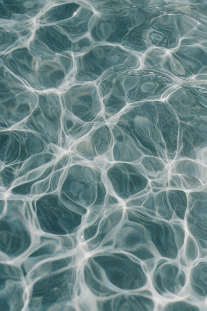 Overhead view of a rippling water surface, intricate network of bright white caustic light patterns, sunlight refracting through fluid, organic interconnected web-like shapes, desaturated teal and slate blue background, shimmering fluid dynamics, gentle waves with distorted reflections, soft ambient lighting, abstract minimalist composition, subtle film grain texture, tranquil atmospheric macro photography