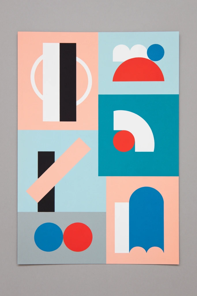 A rectangular abstract geometric print rests on a flat grey surface. The artwork is divided into an irregular grid of solid-colored blocks in pastel peach, light blue, teal, and grey. Nested within these blocks are flat, unshaded geometric shapes in stark white, deep black, bright red, and vibrant blue. These crisp elements include thick vertical and diagonal bars, hollow semi-circles, scalloped arches, and solid circles, creating a high-contrast, minimalist interplay of positive and negative space.