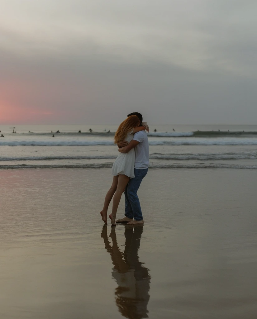 A barefoot couple embraces intimately in the shallow water of a wide, flat beach under a muted twilight sky. The man, wearing a white t-shirt and blue jeans, tightly holds a woman with long reddish-blonde hair in a short white dress, lifting her slightly so her toes just graze the wet sand. Her arms wrap firmly around his neck. The wet shoreline perfectly mirrors their silhouettes. In the distance, gentle ocean waves roll toward the shore, dotted with the tiny dark silhouettes of surfers. The overcast sky blends soft greys with a faint blush of sunset pink near the left horizon, creating a low-contrast, cinematic composition illuminated by diffused, natural lighting.