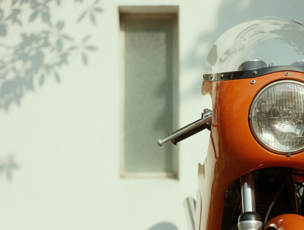 A tight, asymmetrical close-up of a vintage motorcycle positioned on the right edge of the frame. The glossy orange front fairing features a clear, domed windshield and a prominent round headlight with a heavily ribbed glass lens. A single metallic handlebar end protrudes to the left, resting above polished silver suspension forks. The background is a softly defocused, minimalist white wall interrupted by a narrow, recessed frosted glass window. Delicate, dappled leaf shadows fall across the flat white surface, filling the negative space on the left side of the composition. Shot with a shallow depth of field, soft natural daylight, and a warm, retro film aesthetic.