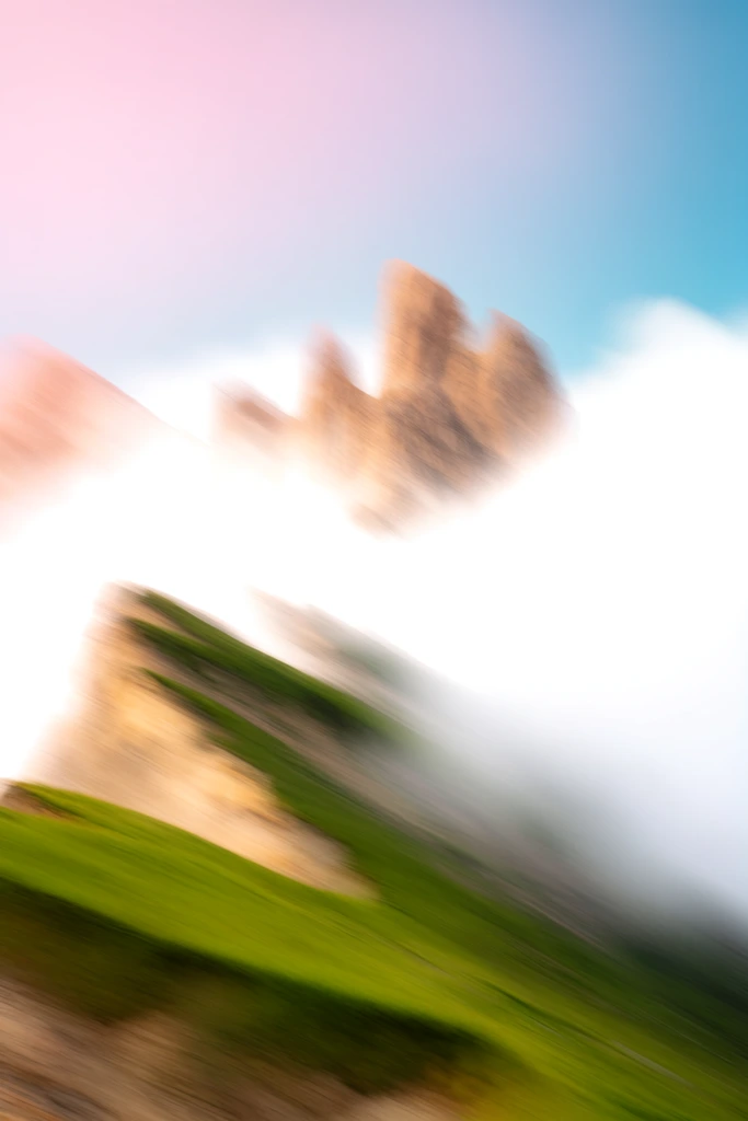 abstracted mountain landscape, heavy motion blur, tan rock peak emerging from bright white cloud bank, green grassy ridges angled diagonally in lower left, intentional camera movement effect, blown-out highlights, pastel pink blue and vibrant green palette