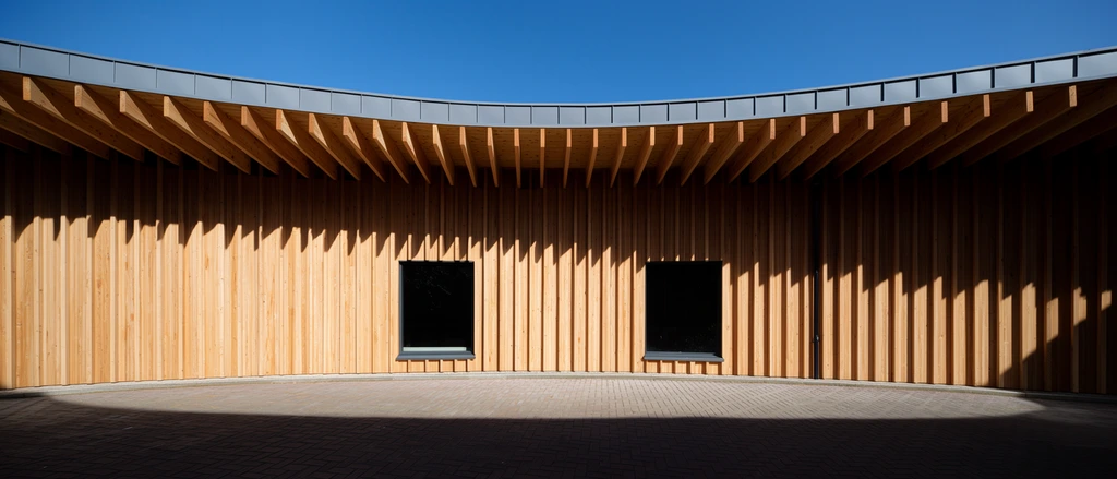Curved architectural facade with vertical light wood slats, overhanging roof featuring exposed beams, sharp jagged shadows cast on warm wood, two dark rectangular windows, grey metal roof trim, interlocking brick pavement, deep foreground shadow, clear blue sky, harsh direct sunlight, minimalist geometry, high contrast architectural photography