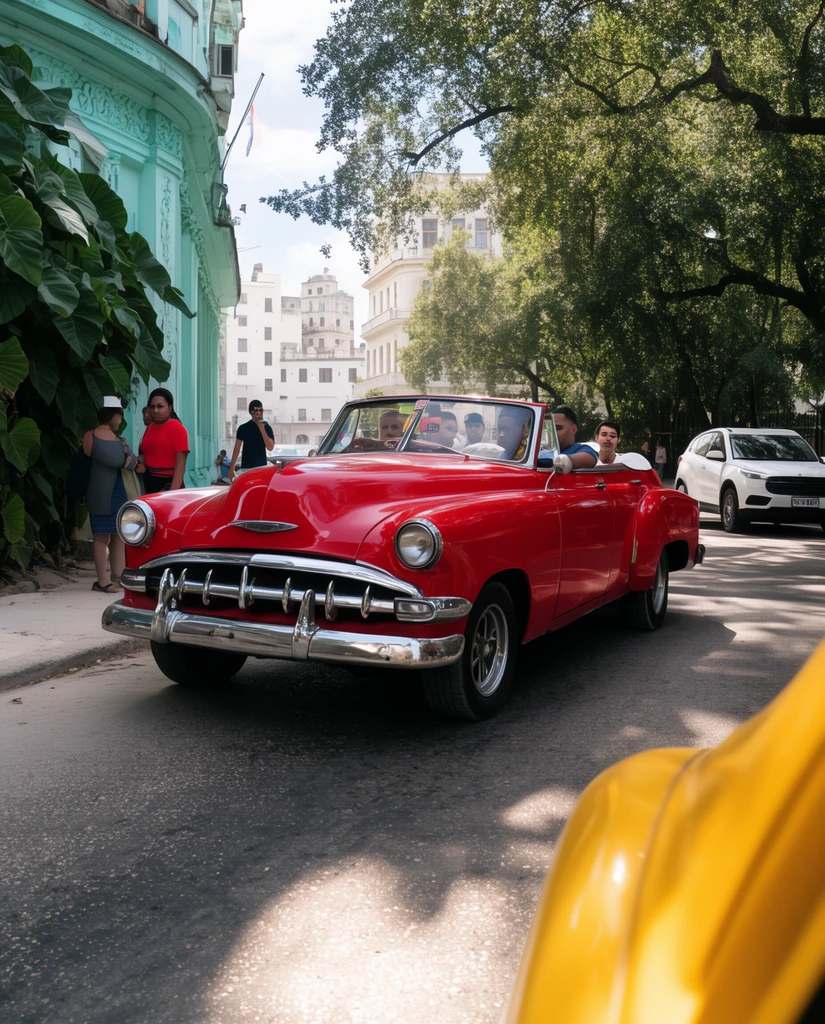 A glossy red vintage convertible with a bright chrome grille drives down a sunlit asphalt city street, carrying several passengers. A blurred yellow car fender occupies the bottom right foreground. To the left, pedestrians stand near an ornate light teal building bordered by large green leaves. A white SUV follows behind the red car, while towering green trees on the right cast dappled shadows across the road and partially obscure distant white multi-story buildings.