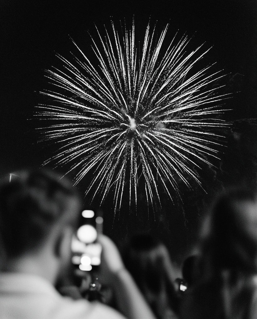 large starburst firework explosion, pitch-black night sky, brilliant white light trails radiating outward, high-contrast black and white photography, heavily blurred crowd silhouettes in foreground, out-of-focus person holding a glowing smartphone, shallow depth of field, film grain