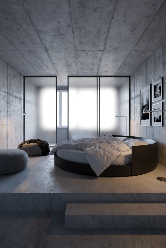 minimalist industrial bedroom, large circular bed with dark curved frame, messy white comforter, elevated concrete platform with steps, raw textured concrete walls, frosted glass panels with black metal framing, diffused backlighting, two grey round poufs, dark blanket draped over one, three framed black-and-white photos on the right wall, sleek metallic floor lamps, brutalist interior design, cool muted grey color palette, photorealistic architectural photography, wide-angle perspective