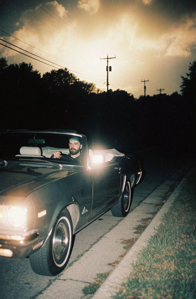low-fidelity 35mm film aesthetic, harsh direct on-camera flash illuminating a man in a vintage convertible car angled left, deep crushed blacks with heavy analog grain, high-contrast foreground isolation, muted vintage color palette, background features a distant road with a curb and grass receding into a pitch-black void, utility poles and a dense tree line silhouetted against an incandescent glowing cloudy sky, eerie surrealist composite look, lo-fi scanned print texture, uncanny mood.