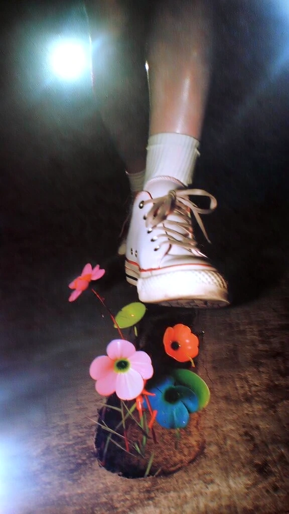 low-angle close-up of a vintage sneaker stepping onto textured charcoal concrete, high-contrast flash photography with heavy vignetting and glossy hotspots, a surreal footprint of vibrant wildflowers and lush green grass emerging from the pavement, 90s film grain aesthetic, raw tactile textures, saturated colors against a dark background, lo-fi indie photography, central composition, ethereal yet gritty juxtaposition, professional cinematic art direction.