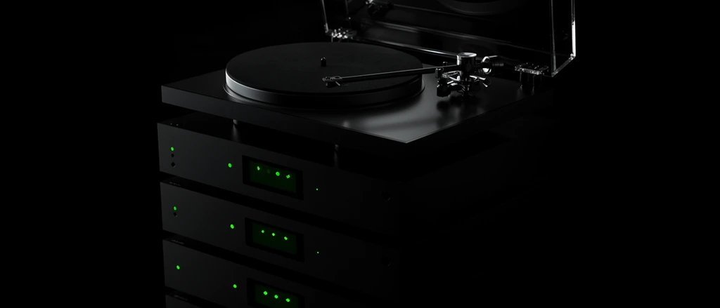 A low-key product shot captures a stack of minimalist audio equipment shrouded in deep shadows. The top features a sleek turntable with a circular black platter, slender tonearm, and a clear acrylic dust cover catching soft reflections. Beneath it, a towering stack of matte black stereo components fades into the dark surroundings. These monolithic front panels are punctuated solely by glowing neon green LED indicator dots and illuminated rectangular interface screens. Staged in a pure black studio environment with dramatic high-contrast lighting, the slightly elevated, angled perspective highlights the glossy mechanical elements of the record player contrasting against luminescent green geometric accents floating in the pitch-black void.