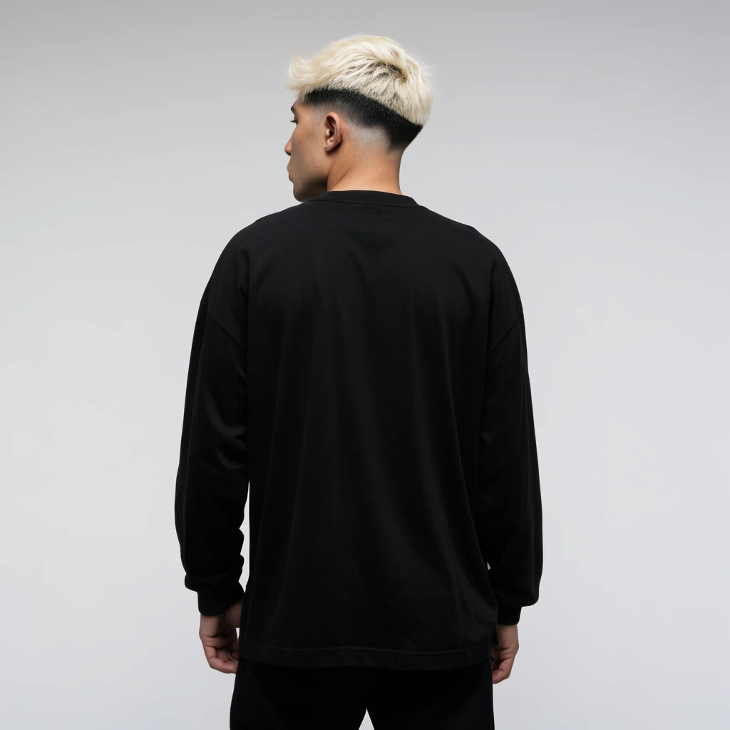 Man viewed from behind, bleached blonde hair with dark faded sides, loose black long-sleeve shirt, black pants, relaxed posture, seamless light grey studio backdrop, soft even lighting, minimalist portrait photography