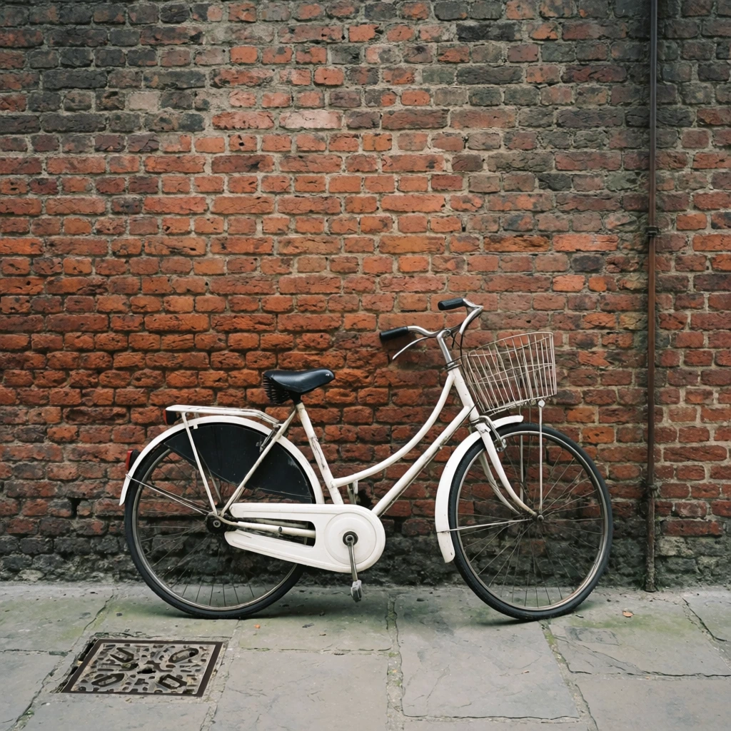 White vintage step-through bicycle parked against an aged red brick wall, curved frame, black saddle, front wire basket, fully enclosed white chain guard, black rear skirt guard, standing on grey stone pavement, dark metal drain cover in the lower left, thin vertical pipe running down the right brickwork, heavily textured terracotta and grey bricks, diffused natural lighting, muted colors, flat straight-on camera angle, wide horizontal composition