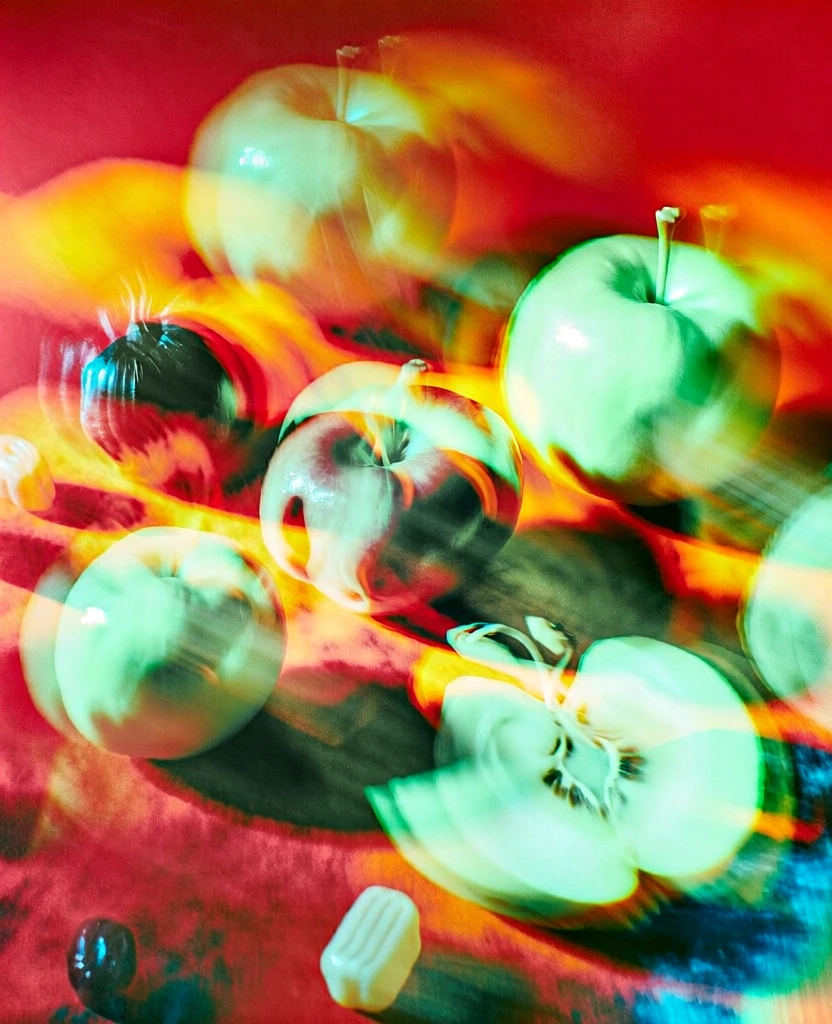 surreal still life of scattered fruits, vegetables, and candies across a field, captured with a hallucinogenic multiple exposure effect, ghosting motion blur, vibrant high-contrast palette of neon greens, incandescent oranges, and deep reds, soft focus glowing highlights, dynamic layered composition, distorted organic shapes, dreamlike atmospheric lighting, chromatic aberration, ethereal glow, cinematic experimental photography style, psychedelic and avant-garde aesthetic.