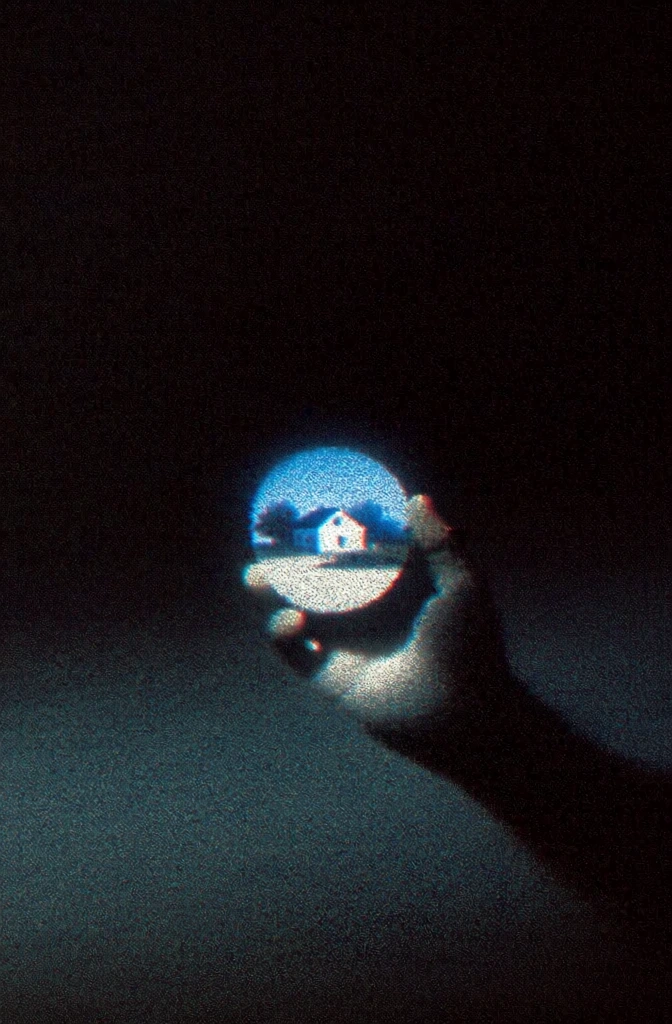 low-fidelity analog aesthetic, high-contrast minimalist composition in a pitch-black void, heavy film grain and digital noise, deep crushed blacks, a hand holds a glowing circular graphic depicting a nostalgic suburban landscape, ethereal blue light emanating from the graphic onto the skin, soft chromatic aberration, tactile vintage texture, surreal liminal atmosphere, muted tones with intense glowing highlights, 1990s retro-media style, grainy cinematic frame