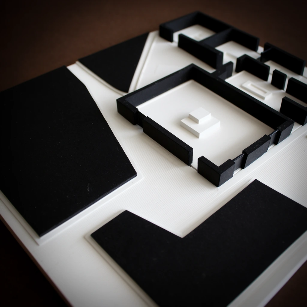 A high-contrast physical architectural floor plan model on a dark brown surface, captured from an angled overhead perspective. Raised geometric shapes form walls and rooms in solid black and bright white. A central white rectangular room is enclosed by thick black perimeter walls with doorway gaps, containing a small stepped platform. Large irregular black polygons dominate the left side and lower foreground. Flat white base surfaces display fine parallel textural grooves. Soft directional lighting casts subtle shadows within the recessed rooms, framed by a shallow depth of field and dark vignette blurring the outer edges.