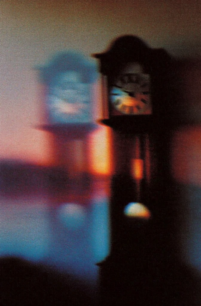 heavy chromatic film grain, lo-fi impressionist smear, extreme soft focus, blurred silhouette of a tall pendulum clock with a visible face and weighted pendulum, positioned next to a ghostly faded outline of its own form, vibrant sunset gradient background of bleeding burnt orange and cyan, high-iso analog noise, painterly light diffusion, halated edges, minimalist composition, ethereal dreamscape, high-signal texture, non-distinct boundaries, nostalgic atmosphere
