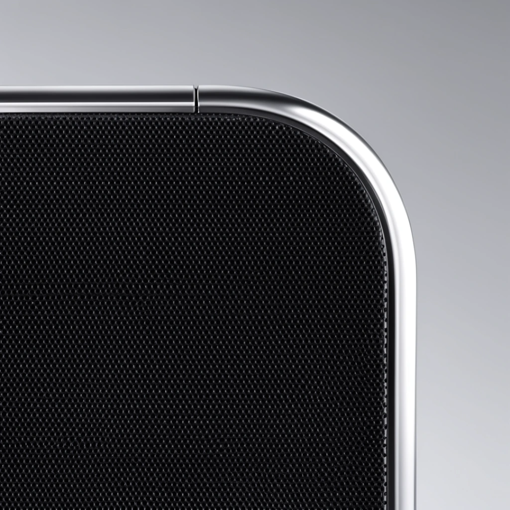 A close-up macro photograph detailing the top right corner of a sleek electronic device. A deep black, finely perforated mesh surface dominates the view, contrasting sharply with a smooth, metallic silver rounded edge catching bright studio highlights. A subtle vertical seam splits the top metallic rim. The object is isolated against a seamless, neutral gray gradient background. The pristine composition emphasizes minimalist industrial design through sharp focus, a monochromatic palette, and precise directional lighting.