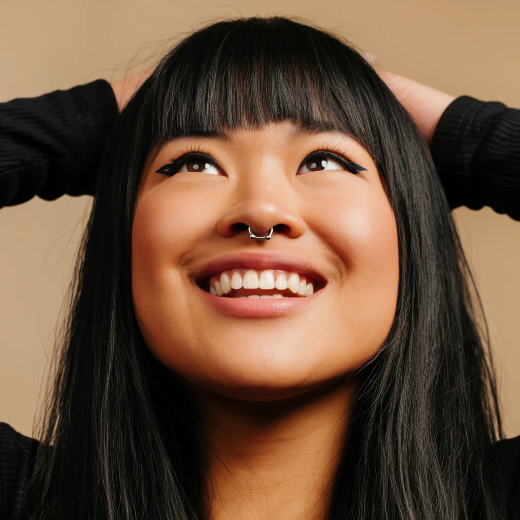 Close-up portrait of a smiling Asian woman looking up, long black hair with straight bangs, silver septum piercing, winged eyeliner, hands resting behind head, black ribbed long-sleeve shirt, plain beige background, warm studio lighting, sharp focus
