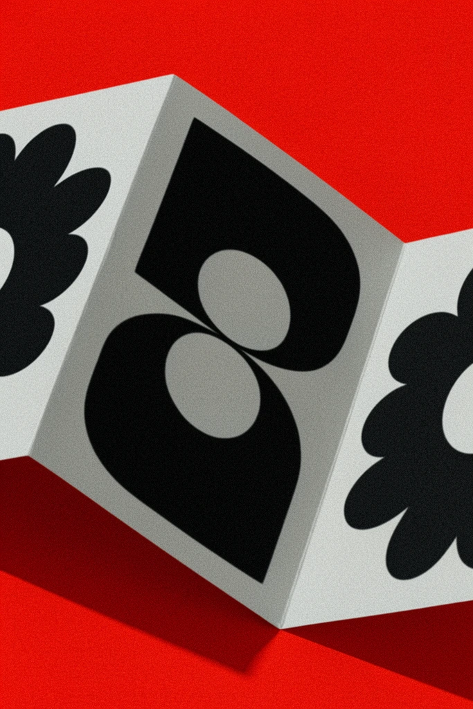 A folded light grey paper card arranged in a sharp accordion zig-zag rests on a vibrant crimson red surface. Bold, oversized flat black graphic shapes are printed across the three visible panels. The central panel features a massive geometric form consisting of thick, curved strokes and two stacked oval cutouts. The flanking panels display portions of abstract, scalloped shapes resembling rounded flower petals with circular negative space at their centers. Intense, angled directional lighting casts deep, crisp geometric shadows from the paper onto the red background, emphasizing the sharp structural folds. The composition is starkly minimalist and highly graphic, unified by a heavy, noisy film grain overlay that adds a gritty, tactile analog texture to the high-contrast color palette of stark black, soft grey, and saturated red.