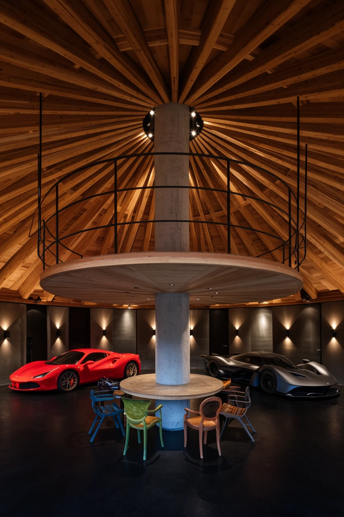 symmetrical circular luxury garage interior, radiating wooden beamed domed ceiling, central concrete pillar with built-in round table, suspended wooden platform overhead, bright red sports car on left, matte grey aerodynamic sports car on right, dark floor, eclectic chairs, warm dramatic spotlights, wide-angle architectural photography