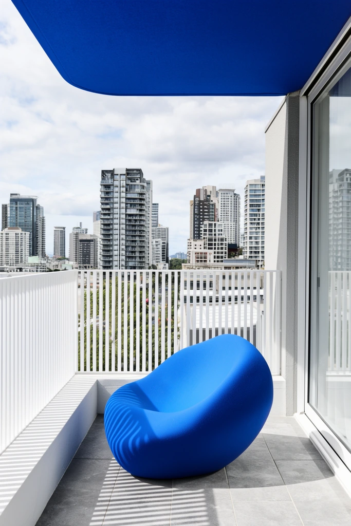 vivid blue organic chair on grey tiled balcony, white slatted railing casting linear shadows, blue overhead shade, urban cityscape with high-rises, architectural photography