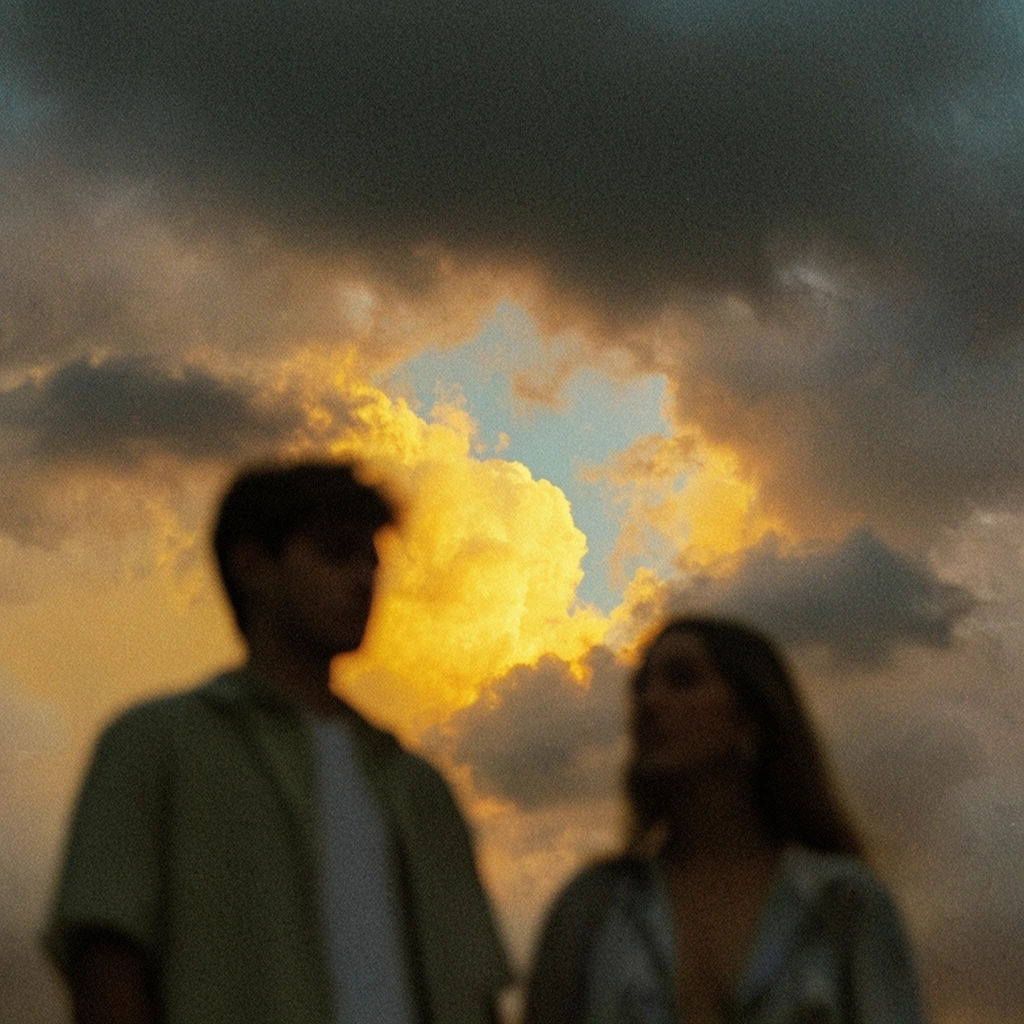 blurred silhouettes of a man and woman in foreground, dramatic sunset sky, heavy dark grey clouds, central opening revealing a glowing golden-yellow cloud, bright sunlight, small patch of pale blue sky, heavy film grain, vintage photographic aesthetic, out of focus foreground, moody atmospheric lighting, low angle