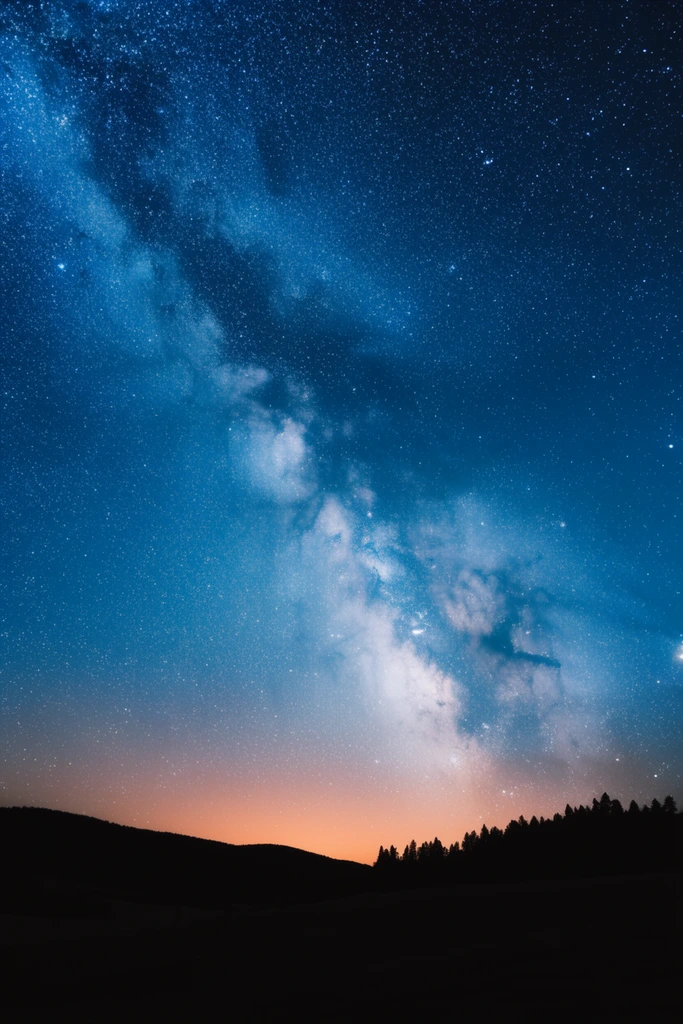 The Milky Way galaxy stretches diagonally across a deep sapphire night sky filled with thousands of brilliant stars. Glowing clusters of pale stellar dust illuminate the vast cosmos. Below, the pitch-black silhouette of rolling hills and a jagged treeline grounds the composition. A soft orange horizon glow contrasts with the cool celestial expanse in this wide-angle astrophotography landscape.