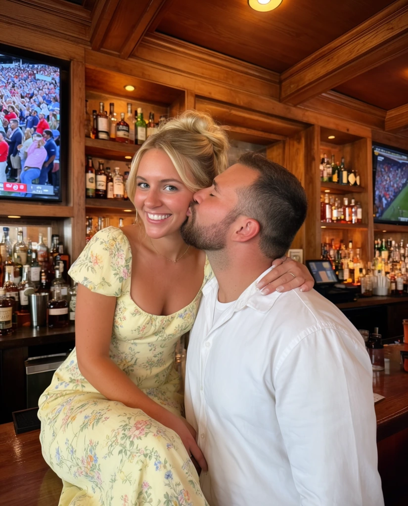 man kissing a smiling woman on the cheek inside a wood-paneled bar, woman seated on the counter wearing a pale yellow floral dress and blonde updo, man in a white shirt with a short dark beard, warm indoor lighting, background of wooden shelves stocked with liquor bottles and a television showing a stadium crowd, candid casual snapshot, vibrant warm colors