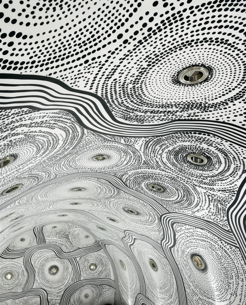 A vaulted white ceiling covered in a high-contrast monochromatic graphic mural of topographical patterns. Thousands of black dots form swirling concentric vortexes, intersected by thick undulating parallel black lines resembling stylized rivers. Circular recessed metallic light fixtures are embedded seamlessly within the curved, visually immersive optical illusion overhead.