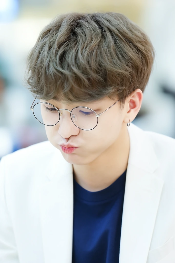 young man looking downward with slightly pursed lips, wavy styled ash brown hair, round wire glasses, white blazer, navy blue t-shirt, small hoop earring, shallow depth of field, soft bright indoor lighting