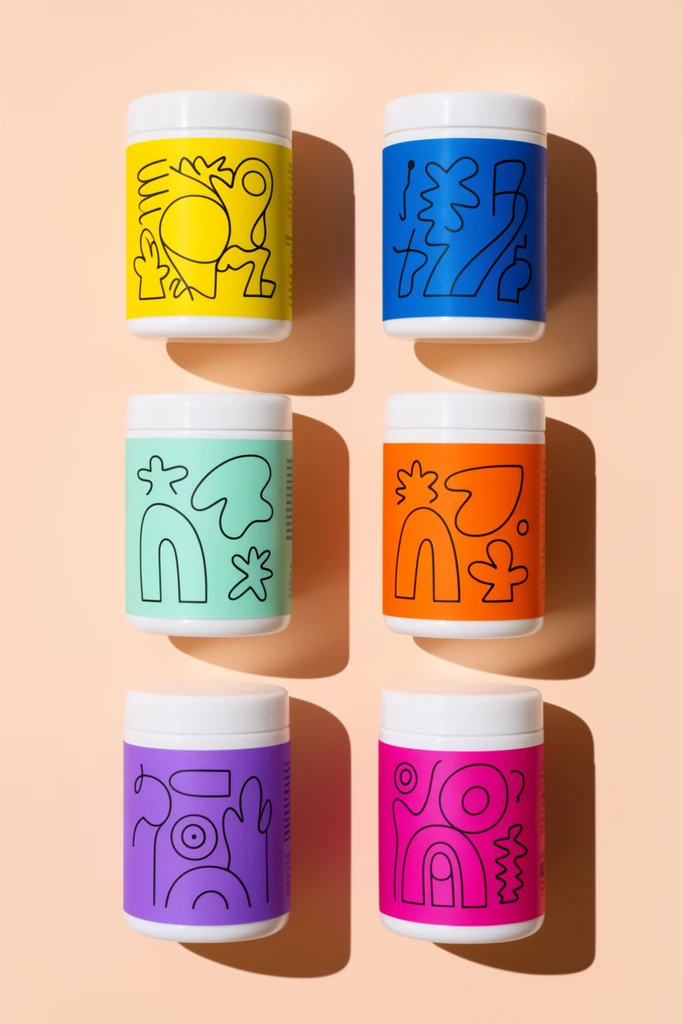 six cylindrical containers in a two-by-three grid, solid pale peach background, flat lay perspective, white caps, vibrant labels in yellow, blue, mint, orange, purple, and magenta, playful abstract black line-art illustrations, hard direct studio lighting, sharp diagonal cast shadows, minimalist product photography, top-down composition