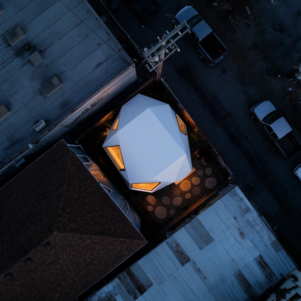 top-down aerial view of a stark white polygonal structure nestled in a dark urban alleyway, warm amber light spilling from its angular windows onto the asphalt, surrounded by contrasting weathered rooftops, dark brown shingle roof, flat gray industrial rooftop, corrugated metal, deep blue twilight atmosphere, heavy cinematic shadows, parked pickup trucks, branching metal utility pole, patio with circular stepping stones, pristine modern geometry against gritty urban textures, moody architectural photography
