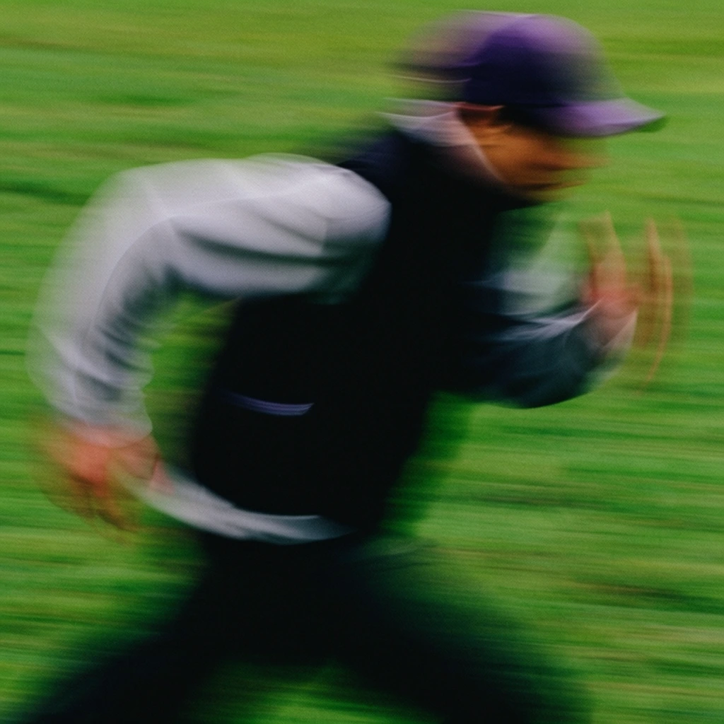 A figure captured in mid-stride racing horizontally across a vibrant green field, heavily abstracted by extreme motion blur. The subject wears a dark purple baseball cap, a black vest over a light gray long-sleeved shirt, and dark pants. The panning camera technique transforms the grassy background into continuous horizontal streaks of vivid green, while the runner's body is smeared into overlapping, translucent shapes of black, gray, and purple. The arms are bent and pumping, and the posture leans aggressively forward, conveying intense speed and dynamic energy. The composition features a grainy photographic texture, emphasizing the kinetic, chaotic feeling of fast-paced movement.