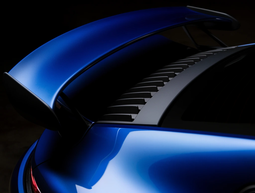 metallic blue sports car rear wing close-up, dark gray engine cover panel with slatted vents, dramatic low-key lighting, sleek automotive macro, deep black shadows, reflective curves