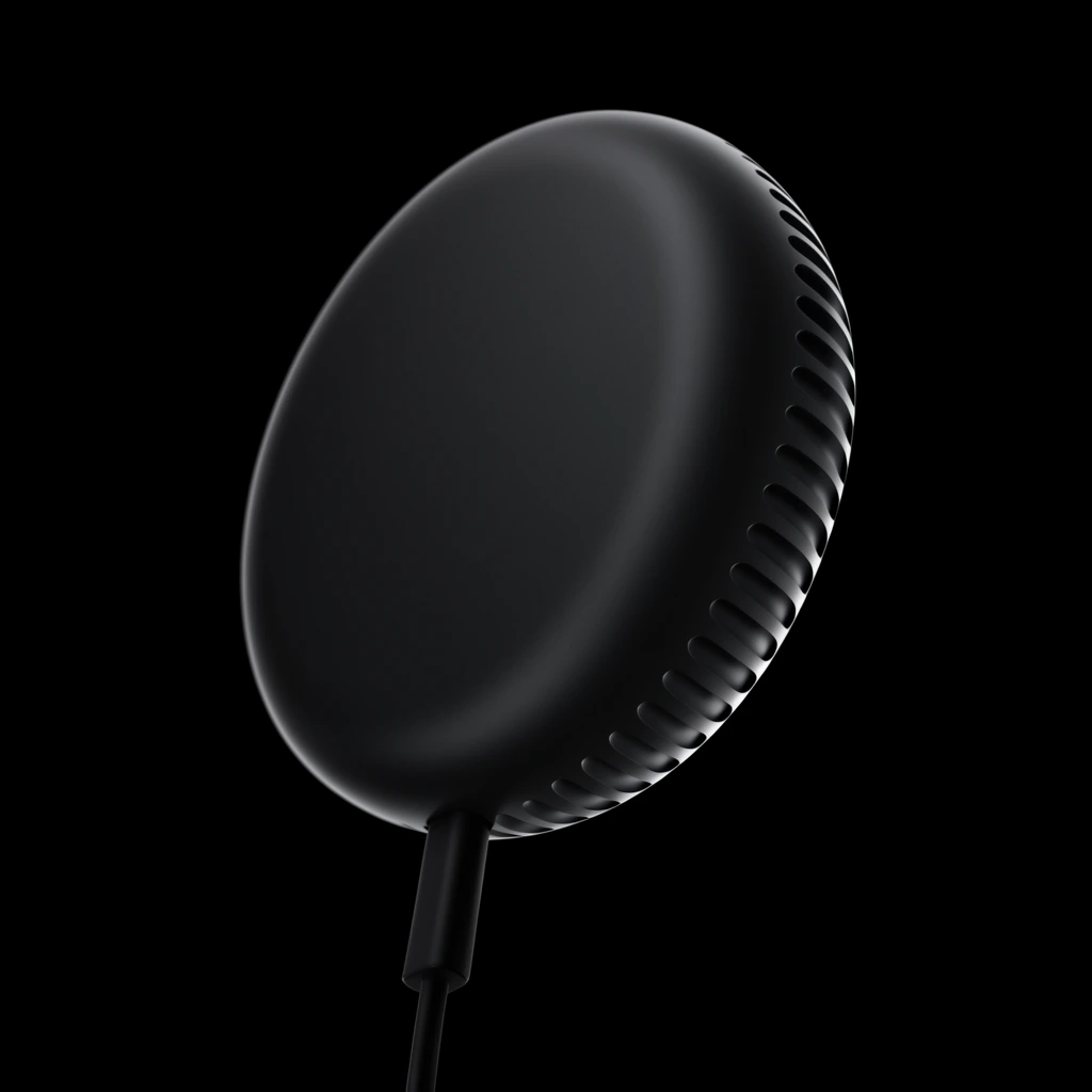 Matte black circular electronic device, sleek puck shape with rounded edges, curved side ventilation slots, attached black cable, pure black background, low-key product photography, dramatic edge illumination