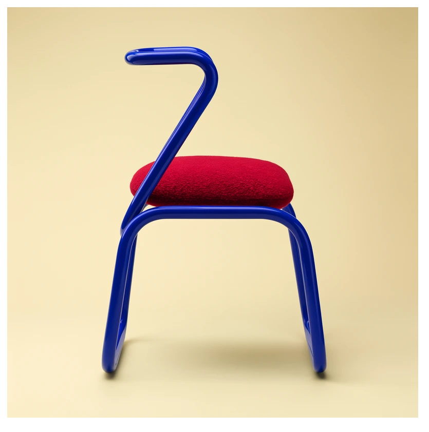 Studio product shot of a sculptural cobalt-blue tubular chair with a deep red cushion, soft cream backdrop, clean minimal composition, crisp reflections.