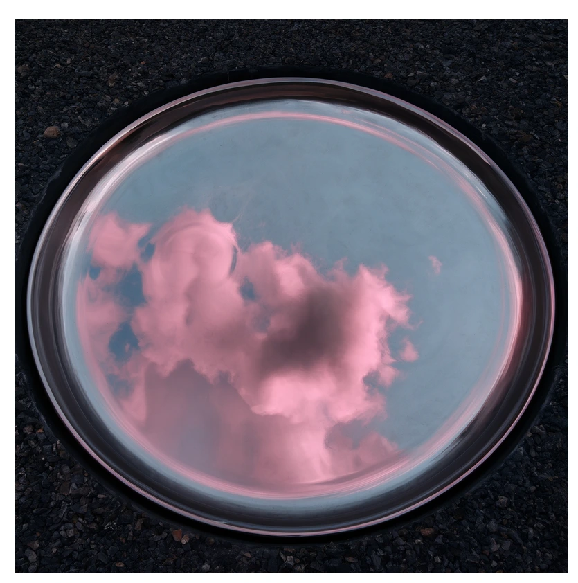 A surreal pink cloud swirling inside a shallow petri dish resting on dark volcanic gravel, conceptual product photography, soft diffused overhead light.